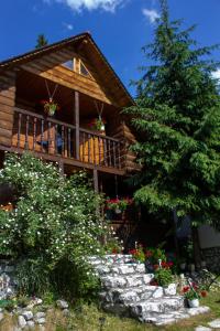 a log cabin with a tree and flowers in front of it at Moara Titului Arieseni in Arieşeni