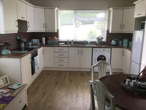 uma cozinha com armários brancos, uma mesa e um lavatório em TJ’s Cottage em Enniskillen