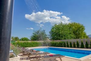 a swimming pool with two chaise lounges next to a fence at Holiday house Anetta with 5 bedrooms in Imotski