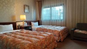 佐世保市にあるレオ プラザ ホテルのベッド2台、椅子、窓が備わるホテルルームです。