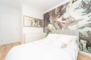 a bedroom with a white bed with a painting on the wall at MIRA APARTMENTS II in Gdańsk