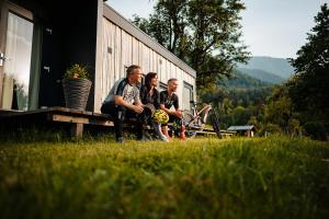 three people sitting on a bench outside of a house at Chaletpark Petzen in Feistritz ob Bleiburg