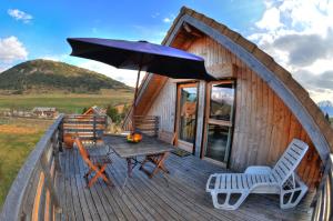 een houten terras met een tafel en stoelen en een parasol bij La cabane du bonheur, un gite écologique 