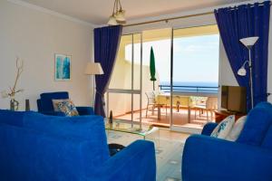 a living room with blue chairs and a view of the ocean at Jardim do Arco "Esmee" in Arco da Calheta