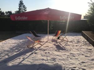 drei Stühle und ein Sonnenschirm an einem Sandstrand in der Unterkunft Hotel zur Post Ochsendorf in Königslutter am Elm