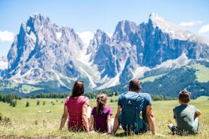 Un gruppo di persone sedute in un campo che guardano le montagne di Lamondis a Castelrotto