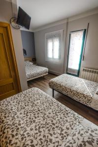 a room with two beds and a tv and two windows at Hostal La Pastora in Candeleda