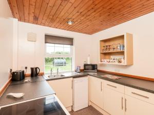 a kitchen with white cabinets and a wooden ceiling at Rose Cottage in Stranraer