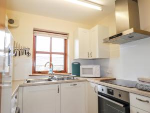 a kitchen with white cabinets and a sink and a microwave at Church House in Poolewe