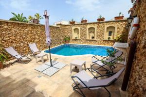 a pool with chairs and an umbrella on a patio at Ta'Ruzar Farmhouse in Xagħra