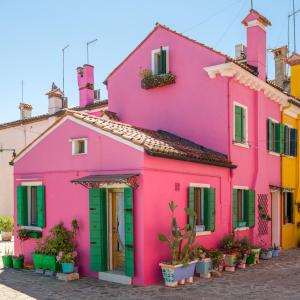 a pink house with green doors on a street at Night Galleria - bed & art in Burano