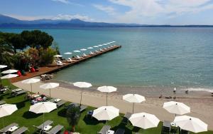 a beach with a row of umbrellas and a pier at Hotel Ocelle Thermae&Spa (Adults Only) in Sirmione