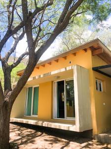 una pequeña casa amarilla con un árbol delante en Cabañas Acaciass en Los Cocos