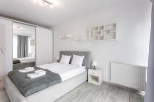 een witte slaapkamer met een groot bed en een spiegel bij Ambria Apartments Flotylla in Świnoujście