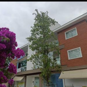 Melhor Apartamento centro Pomerode, perto de tudo في بوميرودي: شجرة أمام مبنى به زهور أرجوانية