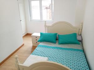 Un dormitorio con una cama con almohadas azules y una ventana en Piso Muxía centro, en Muxía