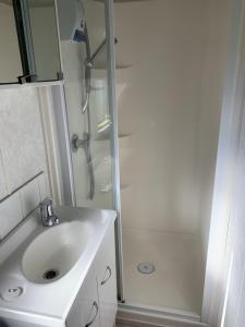 La salle de bains blanche est pourvue d'un lavabo et d'une douche. dans l'établissement Te Puru B8 - 2 bedroom chalet, à Te Puru