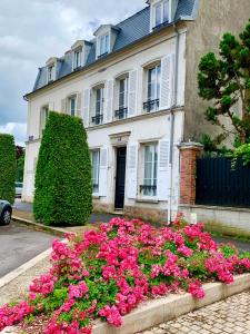 una casa blanca con flores rosas delante en Les Remparts de Joussaume Latour, en Château-Thierry