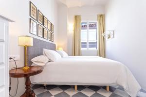 a white bedroom with a large bed and a table at Genteel Home San Laureano in Seville