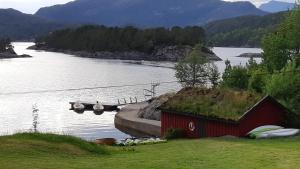 ein rotes Haus mit einem Grasdach neben einem Wasserkörper in der Unterkunft Teigen Leirstad, feriehus og hytter in Eikefjord