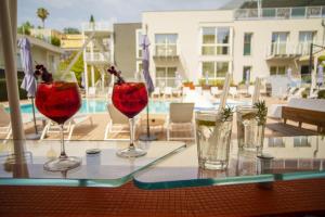 four wine glasses sitting on a table near a pool at Hotel Malavoglia in Acitrezza