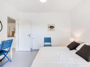 a white bedroom with a bed and a blue chair at Apartment les Terrasses de Capbreton-2 by Interhome in Capbreton