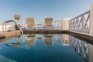 2 chaises assises sur un pont au-dessus d'une piscine dans l'établissement Armeni Village, à Oia