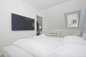 a white bedroom with a bed with a tv on the wall at Ferienwohnung mit Meerblick und Gartennutzung - Haus Inselwind FeWo MEERstrand in Groß Zicker