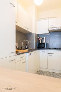 uma cozinha com armários brancos e um lavatório em Hélène, appartement vlakbij het strand em Oostende