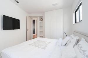 a white bedroom with a bed and a flat screen tv at Hilton Beach by Five Stay in Tel Aviv