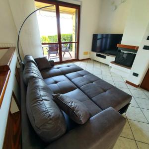 a brown leather couch in a living room with a television at Appartamento Stropea con giardino privato e piscina in Soiano del Lago