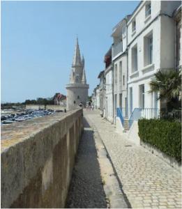 a street with buildings and a lighthouse in the background at Les Remparts, cœur de ville La Rochelle in La Rochelle
