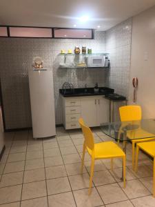 La cuisine est équipée de chaises jaunes, d'une table et d'un réfrigérateur. dans l'établissement Atlântico Flat - Apt 108, à Natal