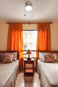 a room with two beds and a window with orange curtains at Hostel Tropical and CoWorking in San Juan del Sur