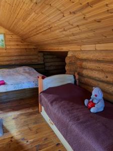 a teddy bear sitting on a bed in a log cabin at Grīnvalti House in Liepāja