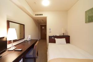 a hotel room with a bed, desk and television at Nest Hotel Kumamoto in Kumamoto