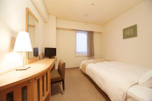 a hotel room with a bed, desk and television at Nest Hotel Kumamoto in Kumamoto