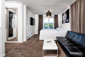 a living room with a black couch and a bed at Hotel 24 Checkin Velden in Velden am Wörthersee