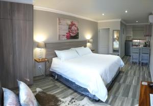 a bedroom with a large white bed and a kitchen at Schnehage Self Catering in Bloemfontein