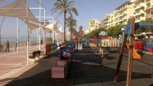 un parque infantil en una playa con palmeras y edificios en Avda España 200, en Estepona