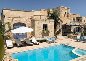 einem Pool mit Stühlen und einem Sonnenschirm neben einem Gebäude in der Unterkunft L'Gharix Temple Retreat in Xagħra
