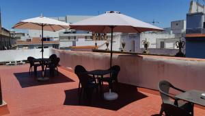 eine Terrasse mit Tischen, Stühlen und Sonnenschirmen auf dem Dach in der Unterkunft Hostel Urban Sevilla in Sevilla