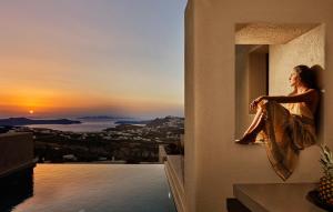 a woman standing on a balcony looking out at the ocean at Halcyon Days Suites in Pyrgos