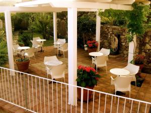 un patio con mesas blancas, sillas y plantas en Hotel Villa Pimpina en Carloforte