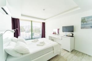 a white hotel room with a bed and a television at GREENBEACH HOTEL in Kalkan