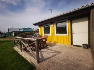 a deck with a table and a yellow house at Susanne's stugor Böda hamn in Böda
