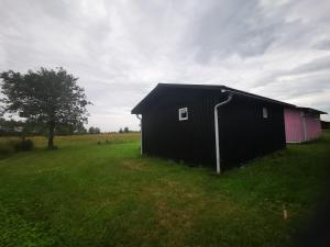 a black building in a grassy field with a tree at Susanne's stugor Böda hamn in Böda