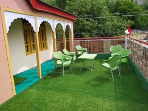 eine Terrasse mit grünen Stühlen und einem Tisch auf dem Gras in der Unterkunft High Cliff Guest House in Khapalu
