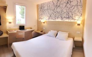 Un dormitorio con una cama blanca y un escritorio y una ventana. en Kyriad Direct Perpignan Nord - Aéroport, en Rivesaltes