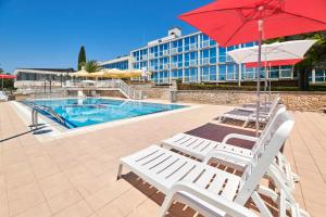 two white lounge chairs and a red umbrella and a pool at Hotel Zorna Plava Laguna in Poreč